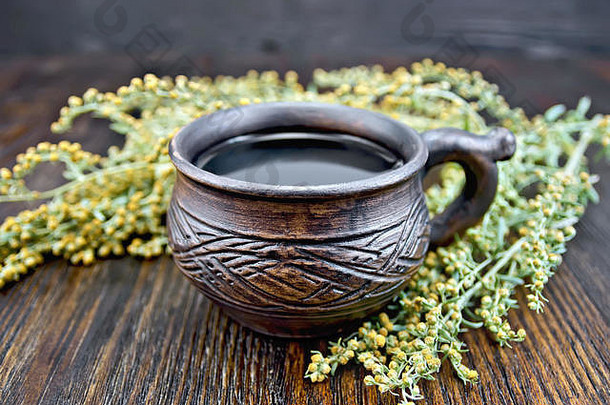 粘土杯中的草药茶，灰色的山艾树枝，在木板背景纸上干燥的艾草