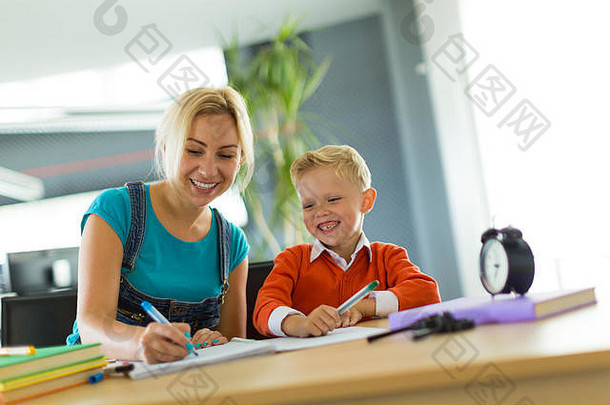 可爱的男孩和女人坐在办公室的桌子旁画画