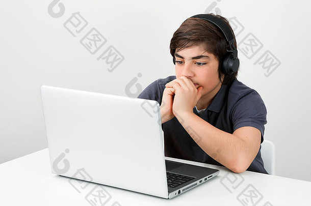 高加索少年戴着无线耳机坐在办公桌旁看着笔记本电脑屏幕。现代教育理念。