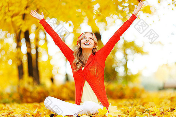 坐在公园秋叶上的快乐年轻女子
