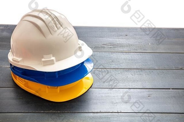 安全生产防护设备。工业防护安全帽白色、黄色和蓝色堆叠在木质背景上。个人健康和安全