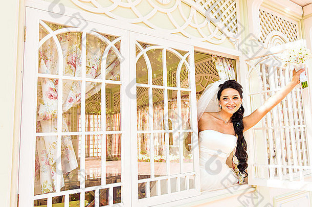 年轻美丽的新娘在窗前等待新郎。美丽的新娘被阳光照亮。美丽的年轻新娘在等待