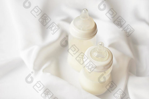 白色丝绸缎子背景上的新生儿奶瓶。免费拷贝空间。顶视图。妇幼保健概念。