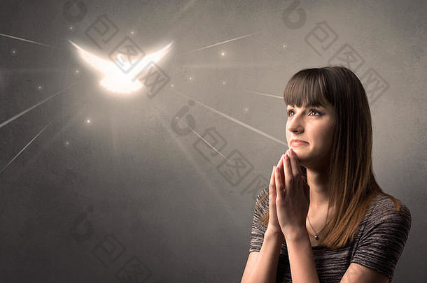 一名年轻女子在灰色背景上祈祷，头顶上有一只闪闪发光的小鸟