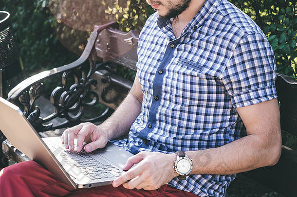 年轻人坐在公园的长椅上，用他的笔记本电脑工作，现代设计笔记本