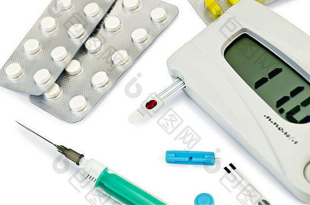 用于测量血糖的灰色仪器，带有白色背景隔离的试纸条、药片和胶囊、注射器、针头