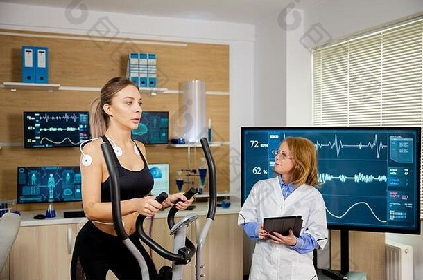 女运动员用电极测试步进机，医生跟着她。运动测试
