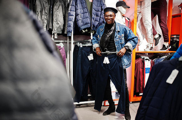 时尚休闲的非裔美国人在服装店穿着牛仔裤夹克和黑色贝雷帽，正在寻找新的运动裤。