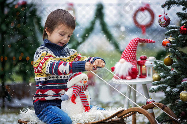 <strong>可爱</strong>的孩子，男孩，坐在圣诞树旁的雪橇上，抱着雪人，冬天下雪