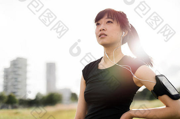 户外拍摄的健身妇女站在城市公园里。穿着运动服戴耳机听音乐的中国女模特杜林