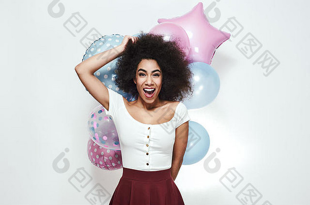 兴奋和幸福。一位年轻的非裔美国妇女手持五颜六色的气球，站在灰色背景下，面带微笑地看着摄像机。党的概念。生日庆典