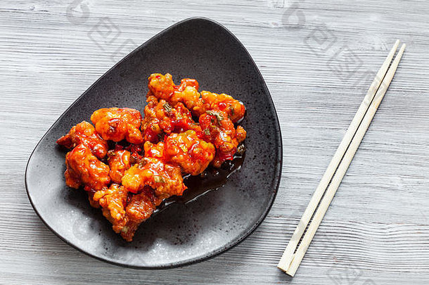 中式<strong>韩国料理</strong>-Kkanpunggi麻辣炸鸡片的俯视图，黑色盘子上放着糖醋酱蔬菜，g上放着筷子