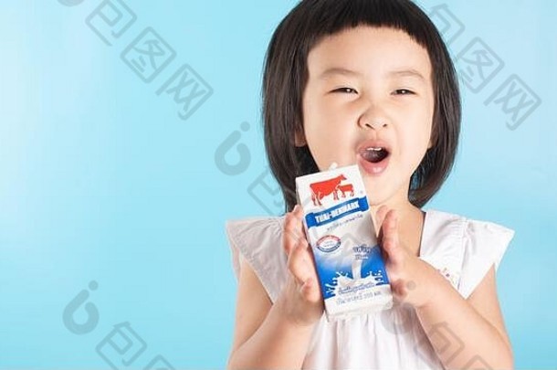 一个可爱的亚洲女孩在蓝色背景和空间里喝着美味可口的天然风味牛奶。