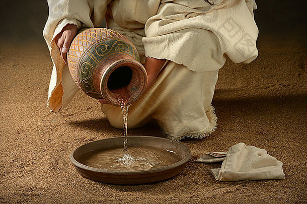 耶稣在黑暗的背景下把水从罐子里倒进锅里