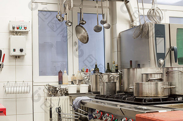 商业厨房内部整洁，壁挂式餐具，中央<strong>燃气灶</strong>上有一系列不同的不锈钢锅