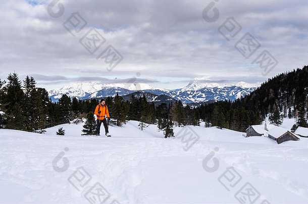 穿着橙色夹克<strong>雪</strong>鞋的男子在霍恩托恩度假胜地的舍伯拉尔姆<strong>雪</strong>鞋上，可以看到霍赫特省雷钦斯坦山脉的恩斯塔尔阿尔卑斯山全景