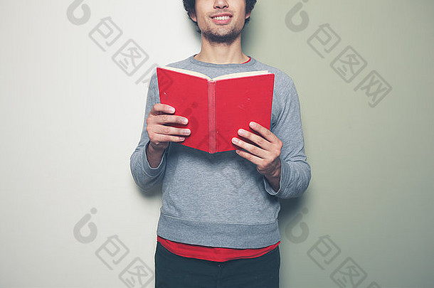 一个年轻人站在黑白相间的背景下，手里拿着一本红色的书