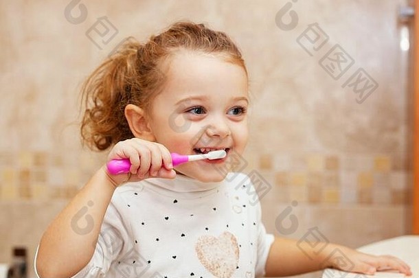 可爱的金发小女孩的肖像，在浴室用刷子和牙膏刷牙。