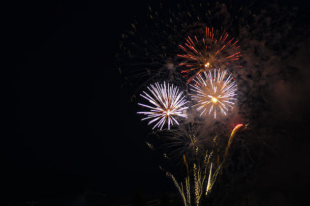 在一个庆祝国庆的夜晚，在黑色天空的映衬下，红色、黄色和白色的绚丽烟火表演。