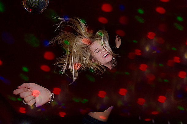 一个金发女孩在镜子球下跳舞，眼睛闭着，沉浸在音乐中
