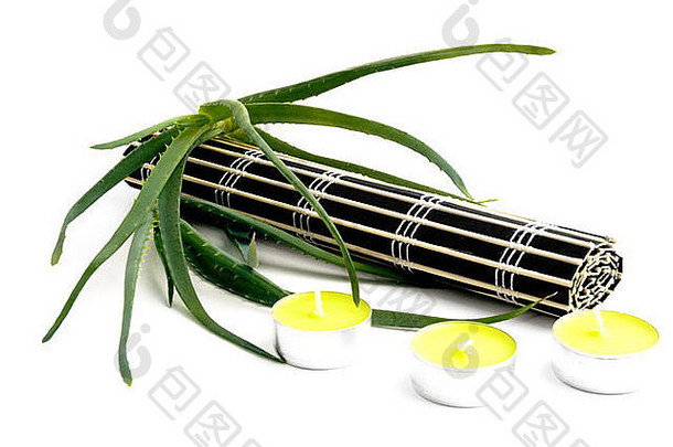 卷曲的黑色竹垫，三根小黄蜡烛和白色背景上的新鲜芦荟。