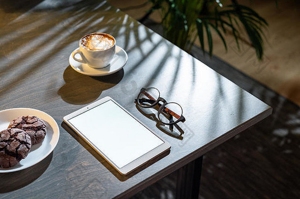 咖啡杯、曲奇饼、玻璃杯和桌面空白屏幕垫的特写镜头。