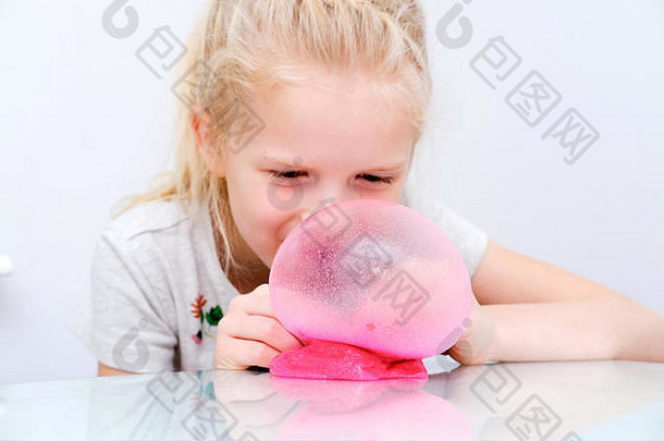 金发女孩用粉色闪光粘液吹泡泡。玩粘液玩具。在家里黏液