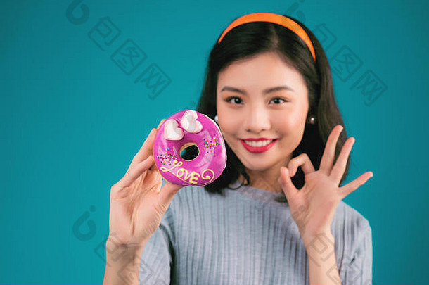 微笑着的可爱的亚洲女人穿着别针式的裙子，拿着甜甜圈在蓝色的上方。