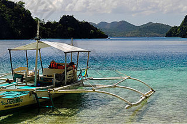 热带岛屿上，蓝色泻湖中的传统菲律宾木船，清澈见底