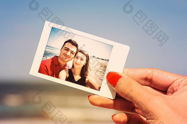 女孩手持有复古的即时照片年轻的快乐夫妇海滩