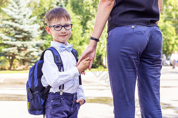 这个男孩是一年级学生，戴着眼镜，手里拿着一个蓝色的公文包