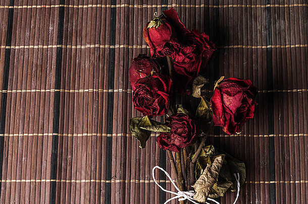用绳子绑着的红色干玫瑰花束。在木制背景上隔离