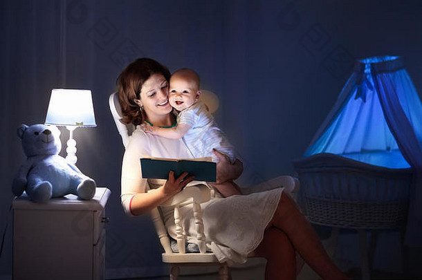 母亲和婴儿在黑暗的卧室里看书。妈妈和孩子在睡觉前看书。晚上和家人在一起。带夜灯的儿童房内部