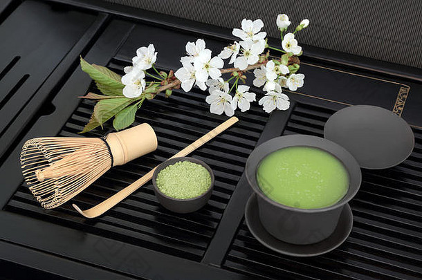 日本绿茶抹茶粉和健康饮料装在杯子里，用搅拌器搅拌，黑色托盘上放着春天的樱花。