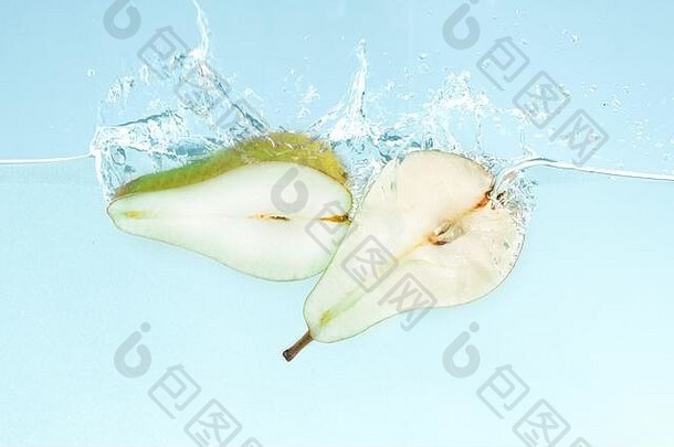 两半美味的绿梨飞入水中，蓝色背景上溅起水花