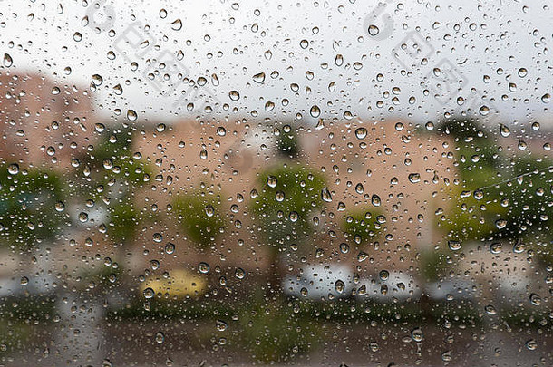雨滴落在住宅的玻璃窗上，背景是城市的一部分