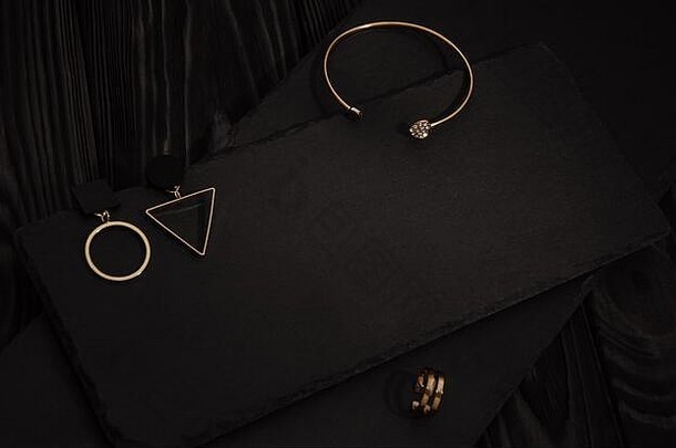 金色手镯、戒指和几何设计耳环，黑色金属板，深色木质背景