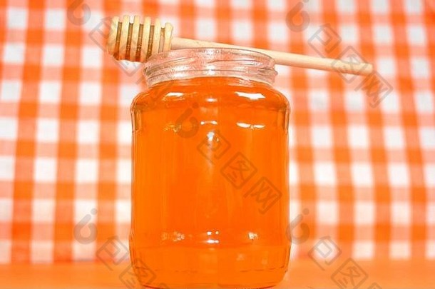 一罐金黄色的蜂蜜和放在<strong>瓶口</strong>的木棍勺。白色和橙格背景，特写，复制空间。