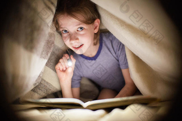 晚上，小女孩在黑暗的房间里用手电筒在毯子下看书