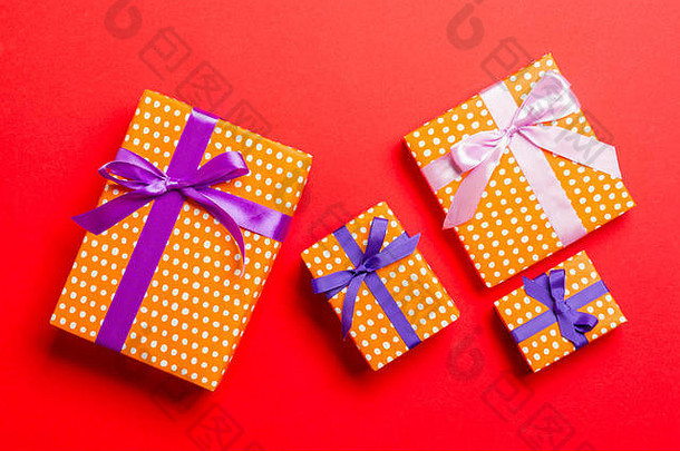 用红色背景上的紫色和粉色缎带用纸包装的圣诞或其他节日手工礼品。礼品盒，彩盒上的礼品装饰