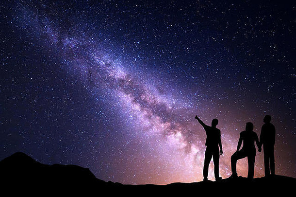 银河系，一个站着的年轻人的剪影在星空中指指点点，他的父母。多彩的夜景。