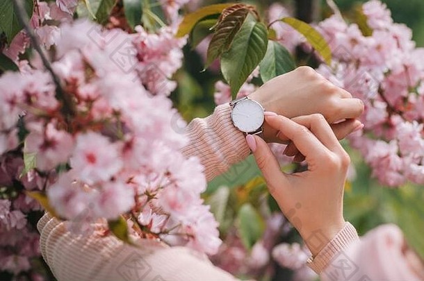 时尚手表，女士手戴，花朵背景。一个女人看着她的手表。