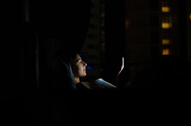 睡前躺在床上的女孩看着智能手机。睡觉前查看新闻和社交网络。智能设备。