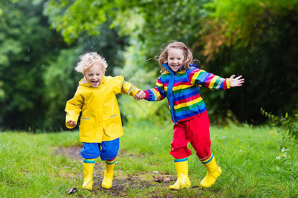 小男孩和小女孩在多雨的夏季公园里玩耍。孩子们穿着五颜六色的彩虹夹克和防水靴，在雨中跳进水坑和泥里。沃尔的孩子们