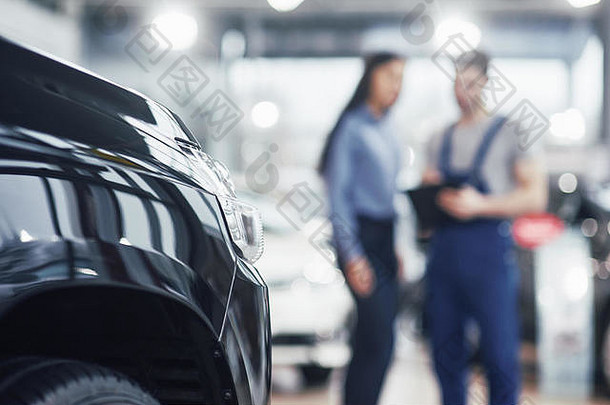 美丽的年轻女子在经销商处修理汽车时正在和英俊的汽车修理工交谈