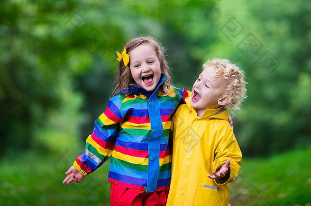 男孩女孩玩多雨的夏天公园孩子们色彩斑斓的彩虹夹克防水靴子跳水坑