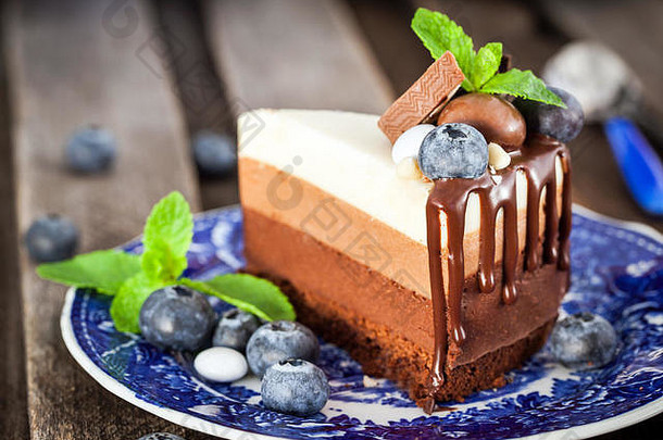 一块美味的三巧克力<strong>慕斯</strong>蛋糕，饰以新鲜蓝莓、薄荷和糖果