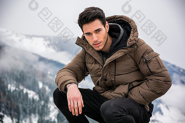 穿着外套的帅哥坐着看镜头。背景上的雪景