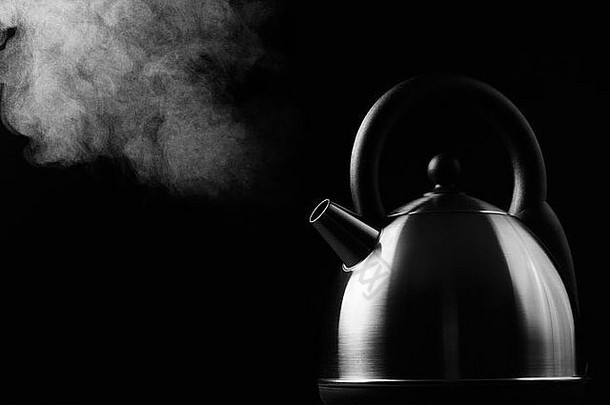 热的现代水壶在黑色背景上沸腾，蒸汽升到光亮处