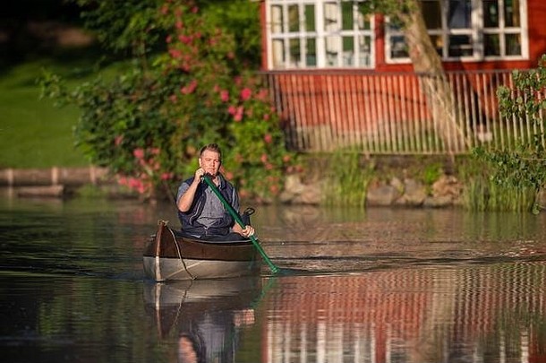 清晨，一名男子坐在独木舟上，在金色的阳光下，在一条河上骑行
